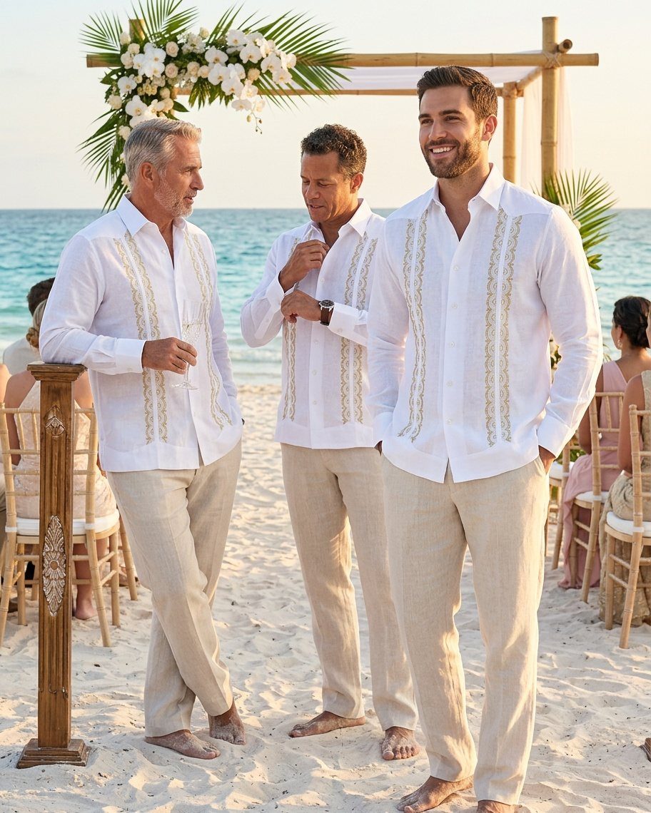 Three men in white embroidered shirts and beige linen pants standing on a beach.