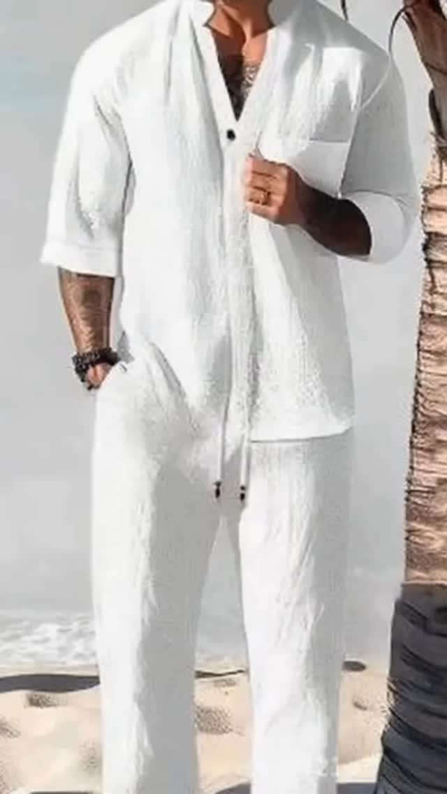 Man in a white linen short-sleeved shirt and matching trousers standing on a beach.