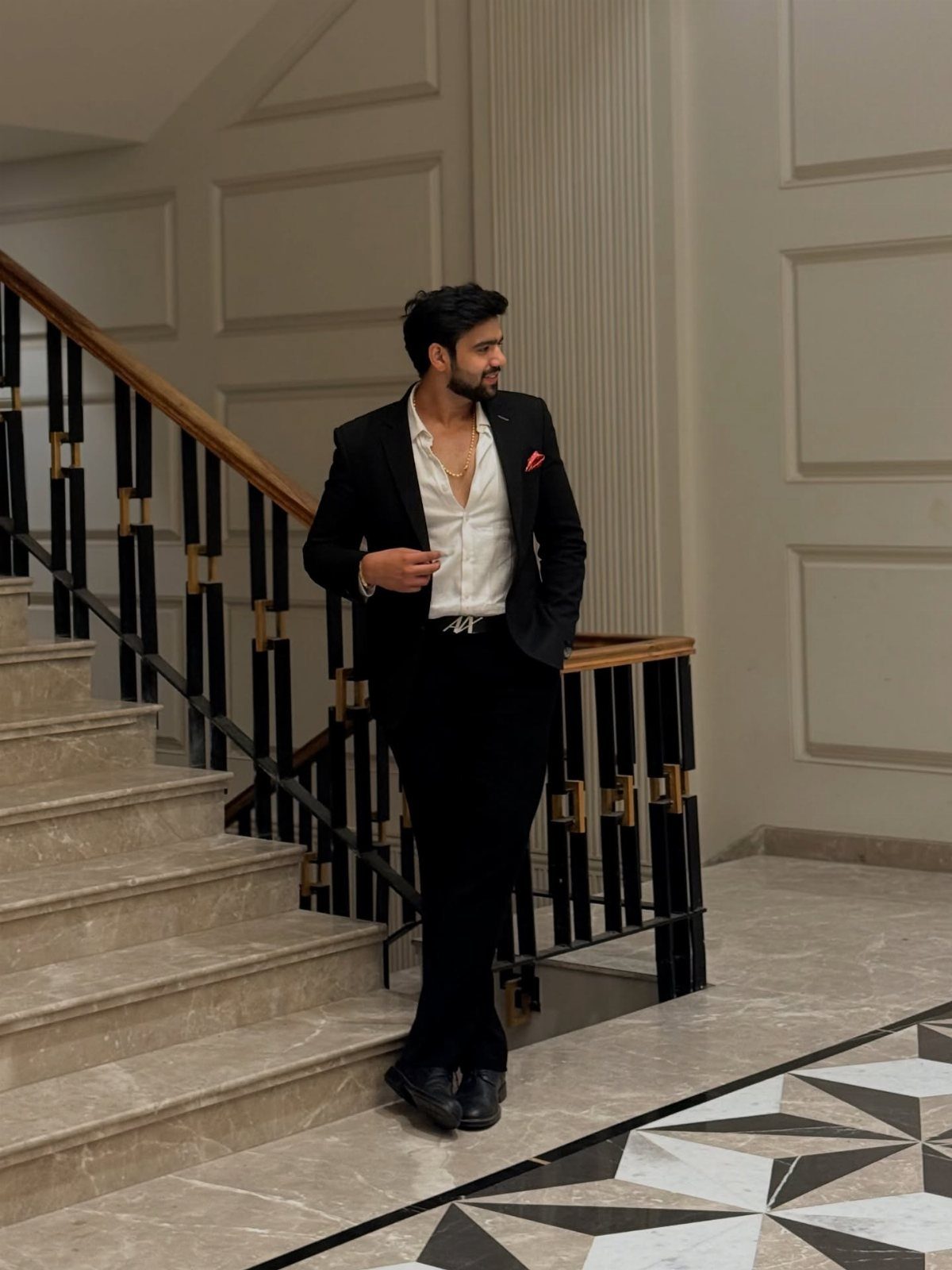 Man in a black blazer and white dress shirt posing on a staircase.