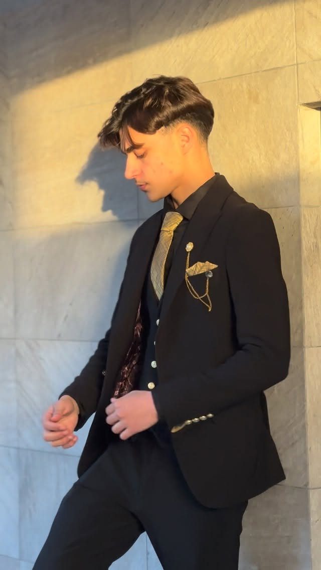 Young man in a black suit featuring a gold patterned tie and decorative pocket square.