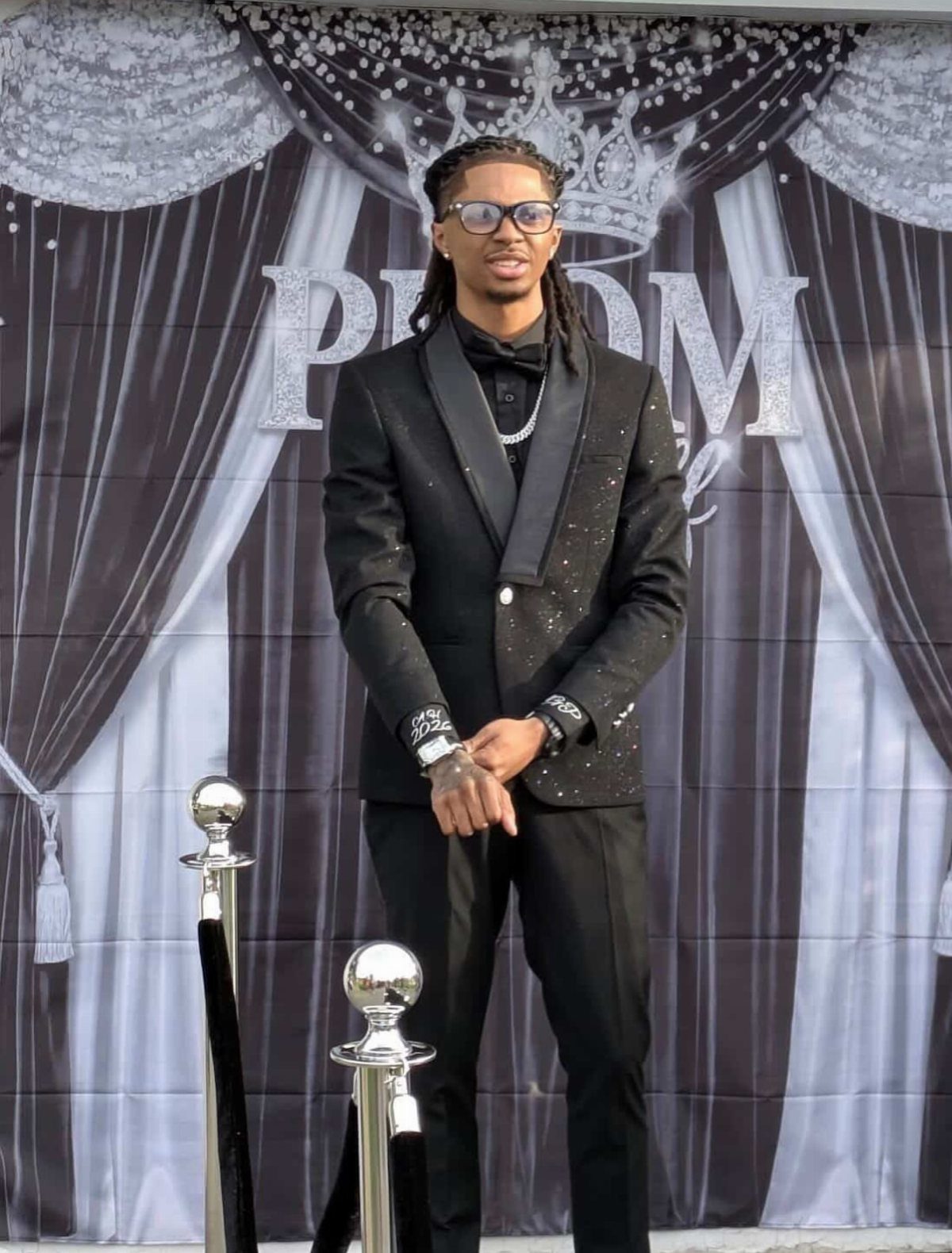 Young man in a black suit and bowtie posing in front of a prom backdrop.