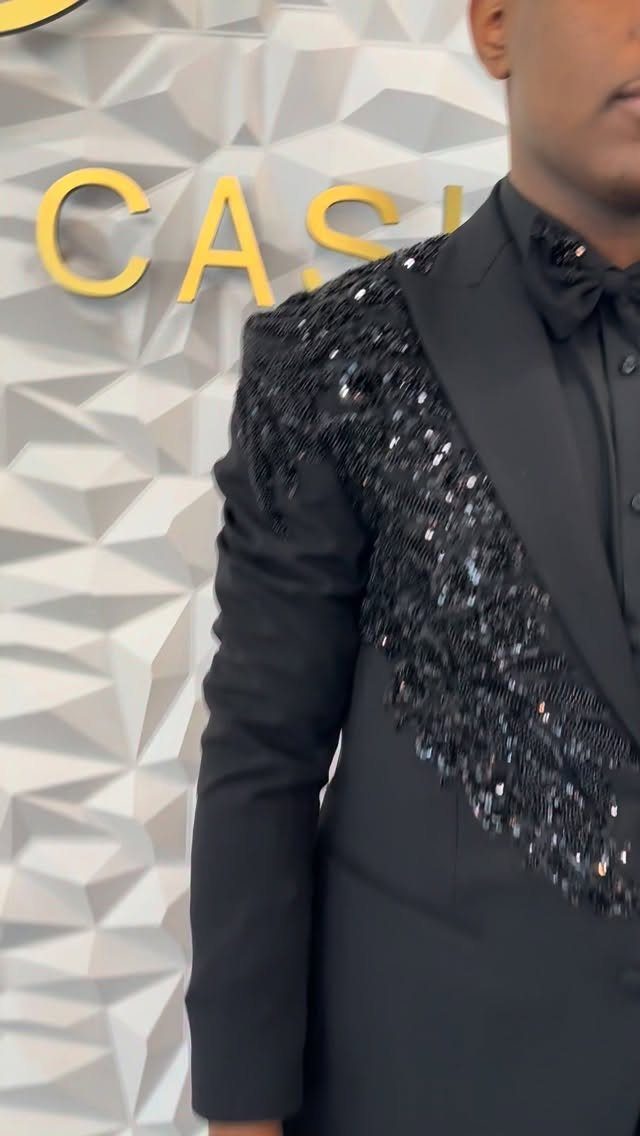 A man wearing a black suit with sparkling black sequins on the shoulder and lapel.