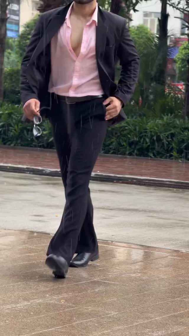 Man walking in a black suit paired with a light pink shirt.