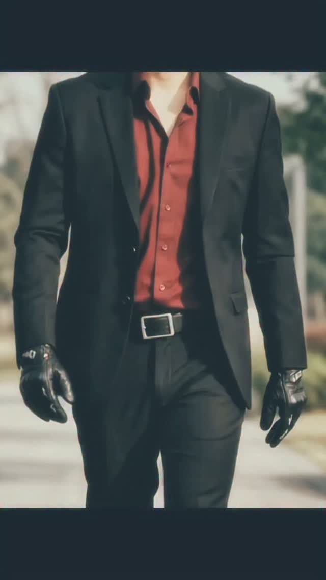A person wearing a black suit, a dark red shirt, and black leather gloves.