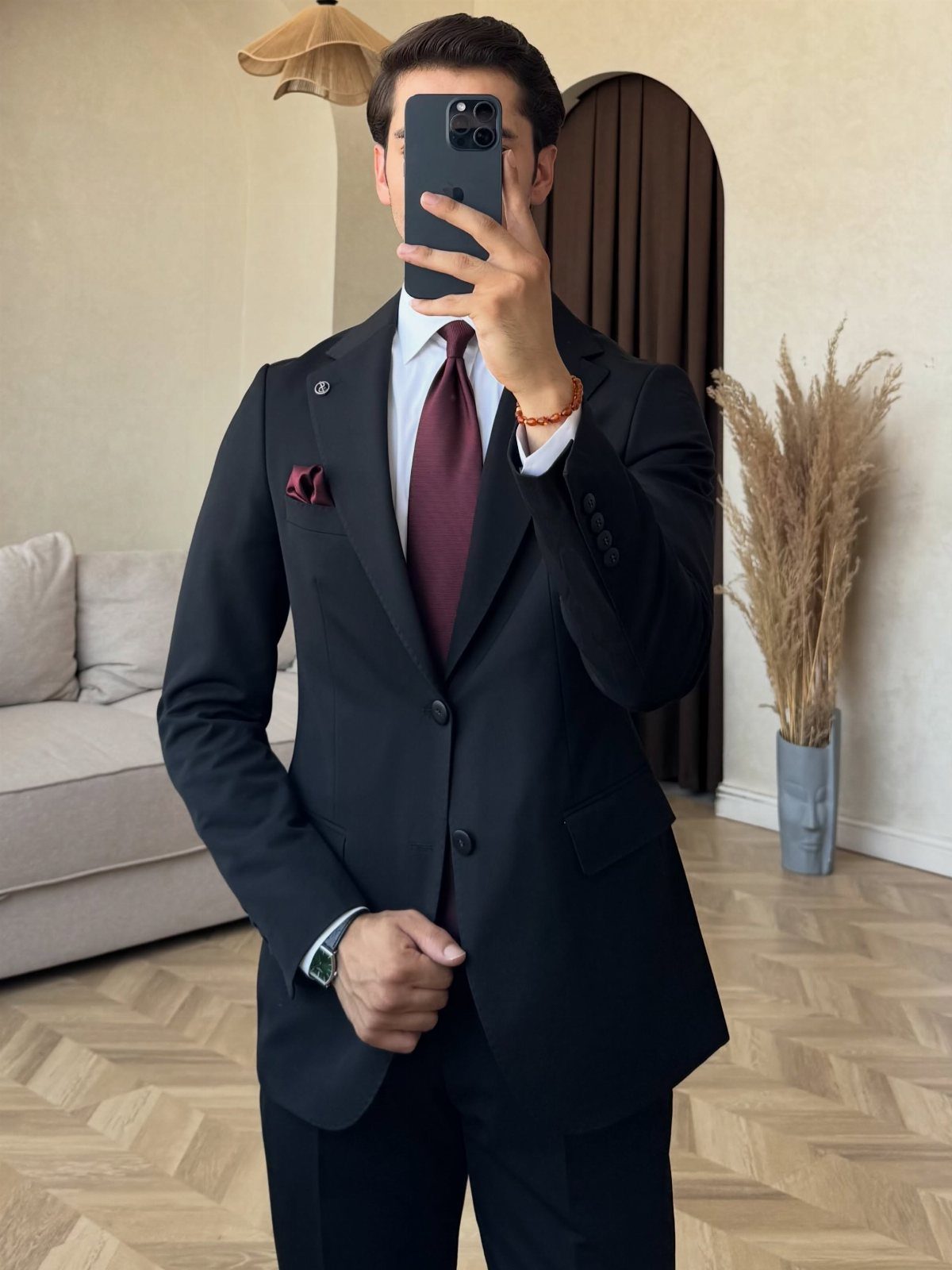 Man wearing a black suit with a white shirt and a burgundy tie taking a selfie.