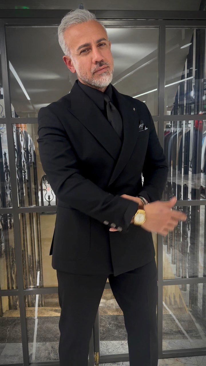 Man with grey hair wearing a black suit, black shirt, and black tie.