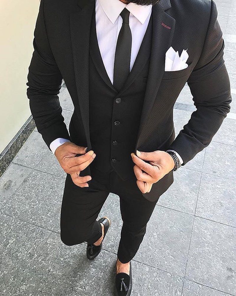 Man in a black three-piece suit with a black tie and white pocket square.