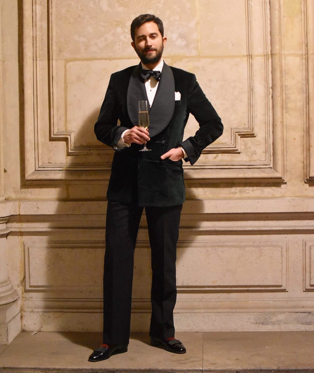 Man in a black velvet dinner jacket with a grey shawl collar holding champagne.