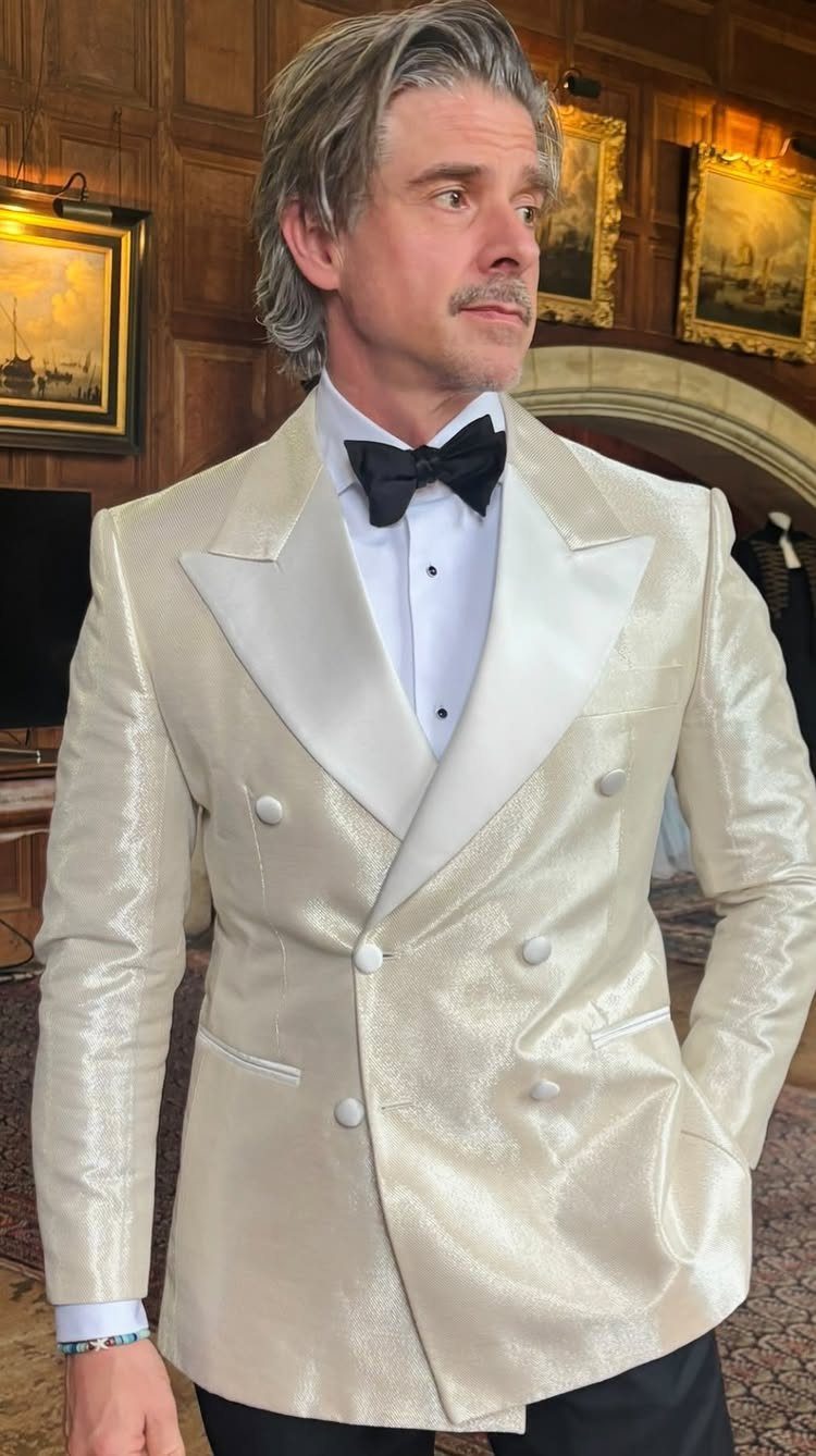 Man wearing a cream textured double-breasted tuxedo jacket with white satin lapels and a black bow tie.