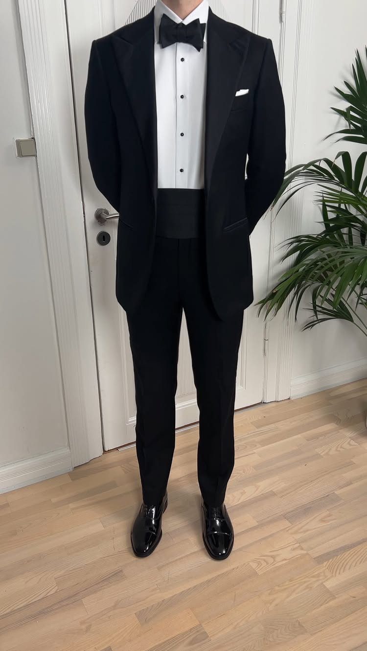 Man in a black tuxedo featuring a white shirt, black bow tie, and a wide black cummerbund.