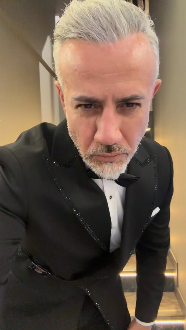 Man with styled grey hair and a neat beard wearing a black tuxedo and bow tie.