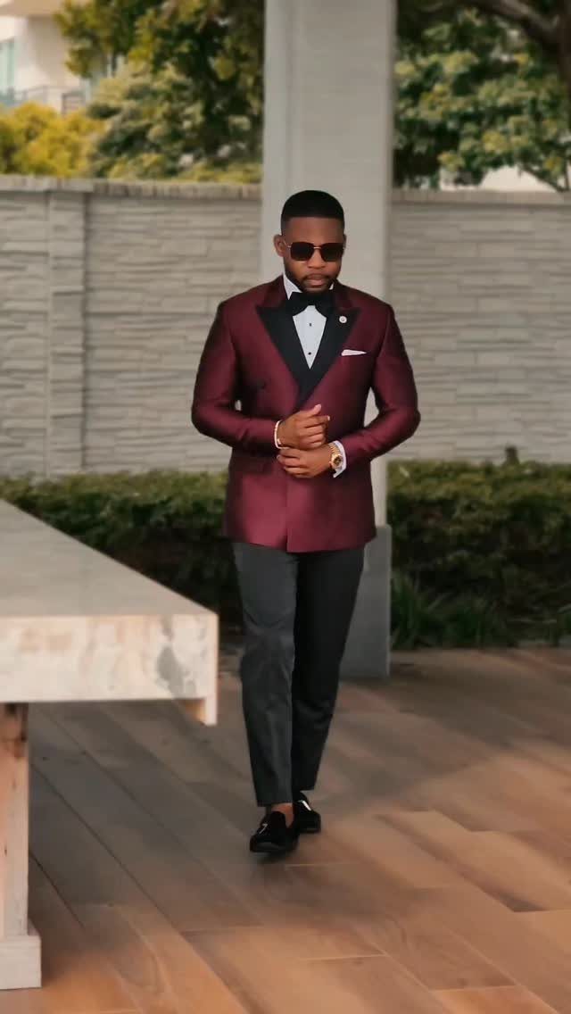 Man in a maroon tuxedo jacket, black bow tie, and dark trousers walking outdoors.
