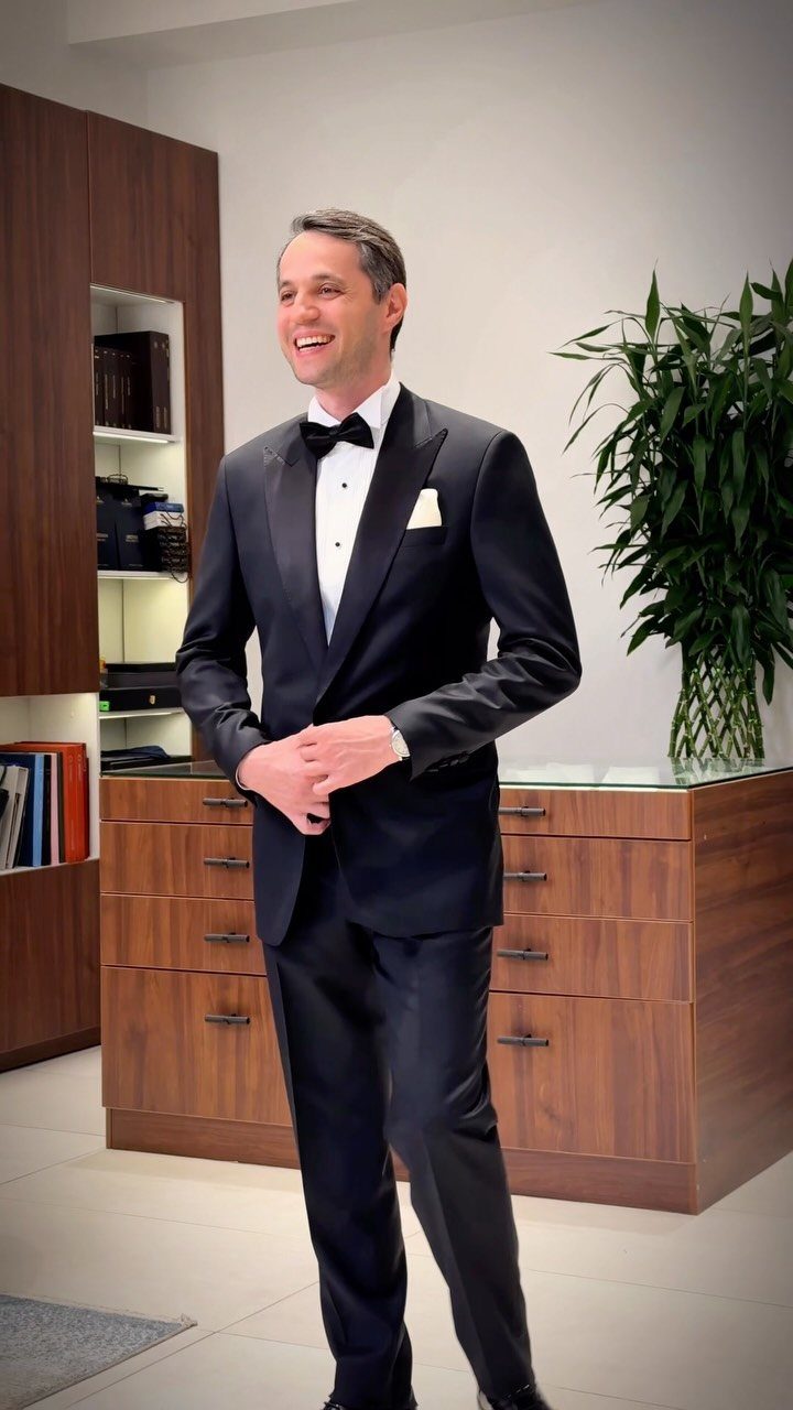 Smiling man in a black tuxedo with a white pocket square and black bow tie.