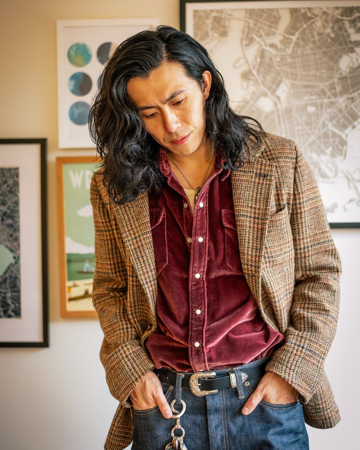 Man wearing a patterned brown blazer, maroon velvet shirt, and dark denim jeans.