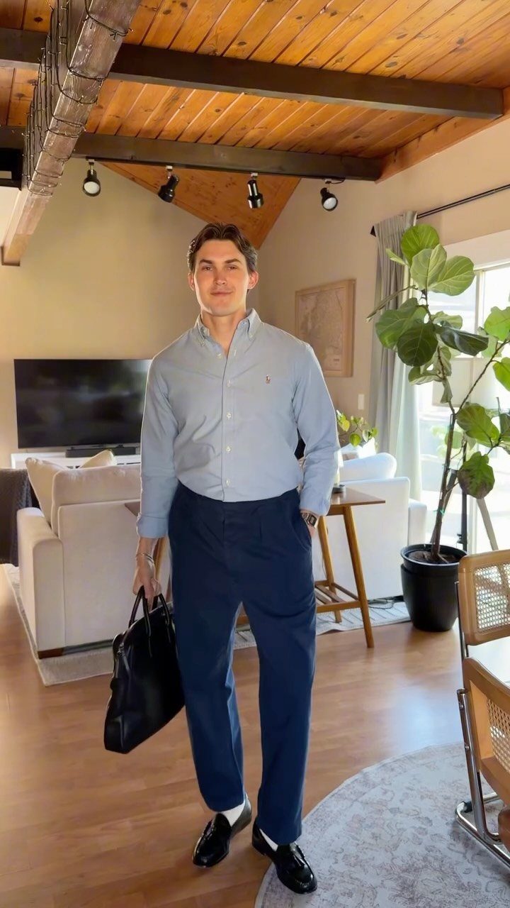 Man standing in a living room wearing a light blue shirt and navy blue chinos.