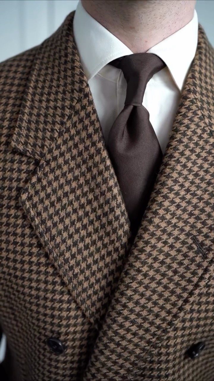 Man wearing a houndstooth blazer, white shirt, and brown necktie.