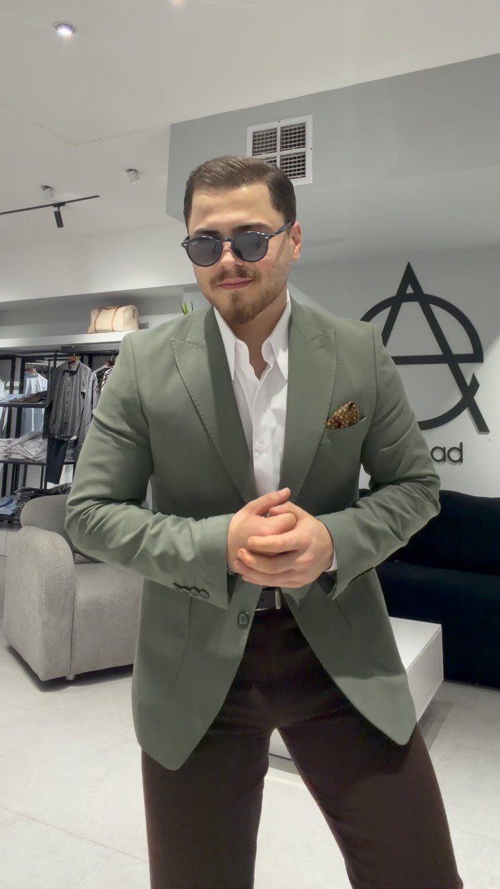 A man in a sage green blazer and brown trousers posing in a store.