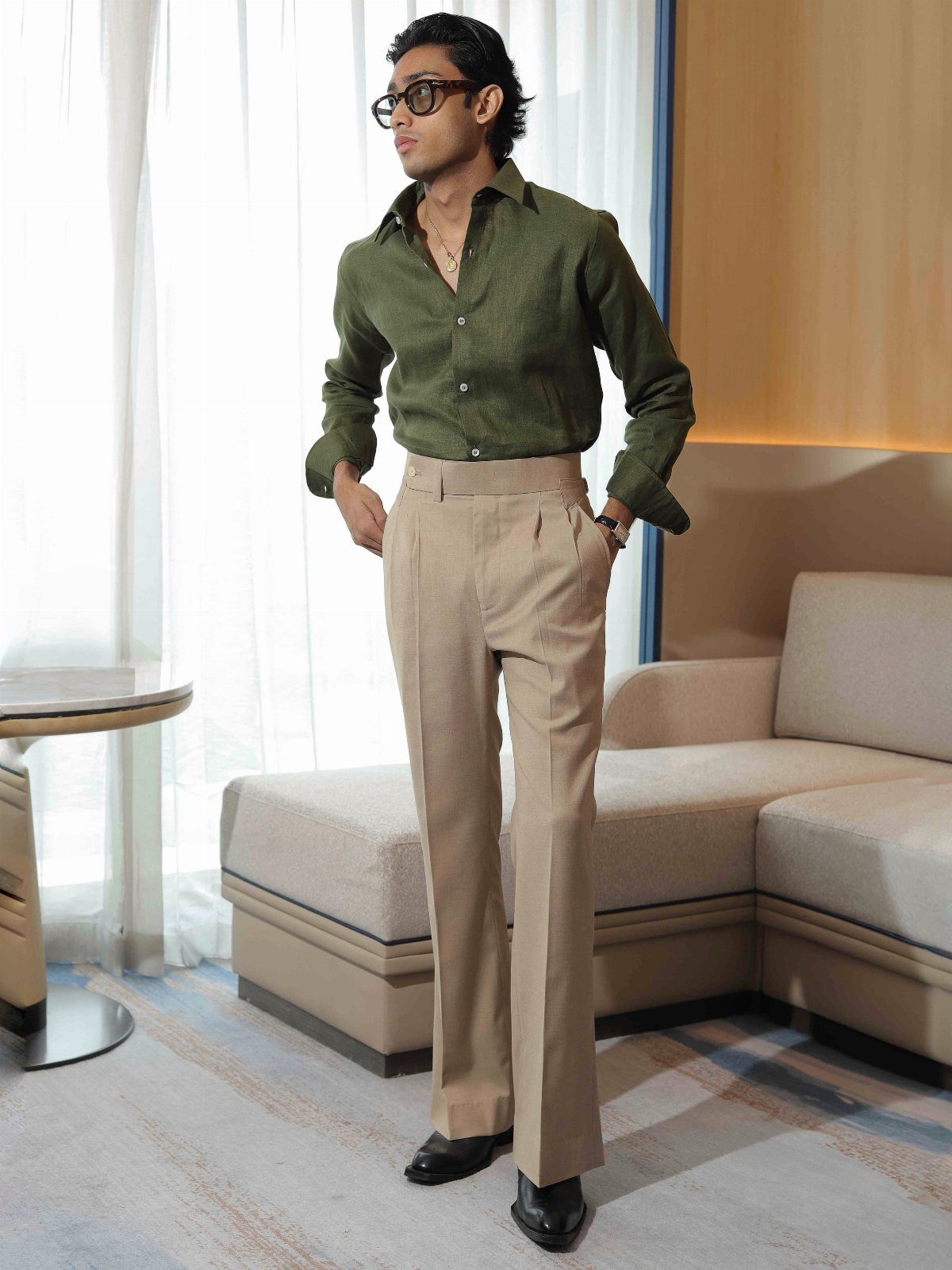 Man in olive green shirt and tan trousers standing in a modern living room.