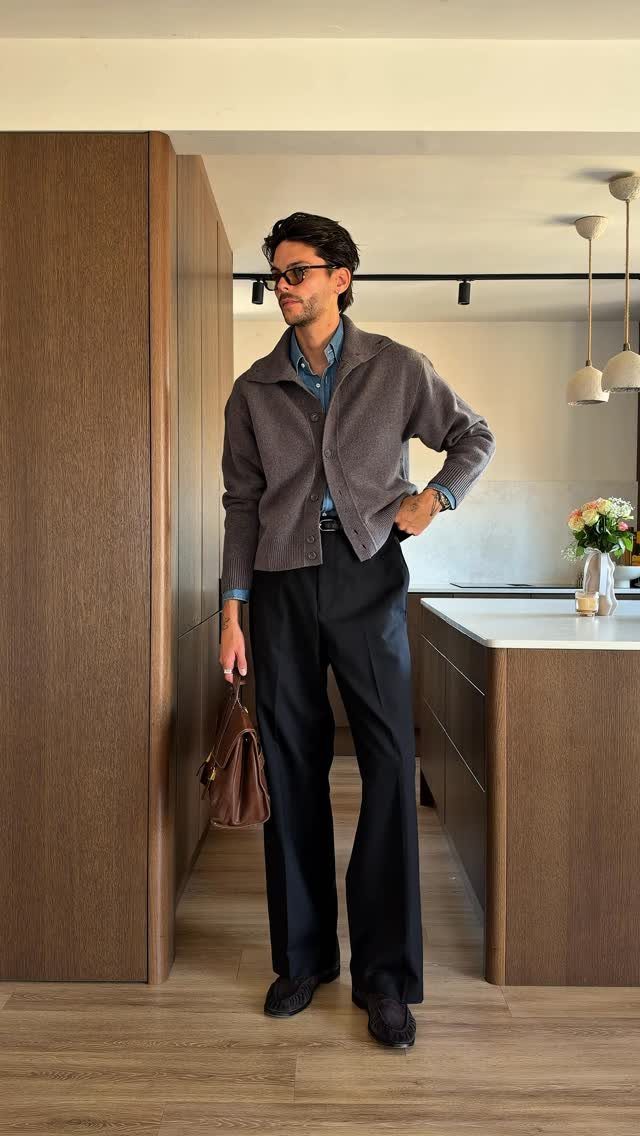 Man in a grey cardigan and blue collared shirt standing in a modern kitchen.