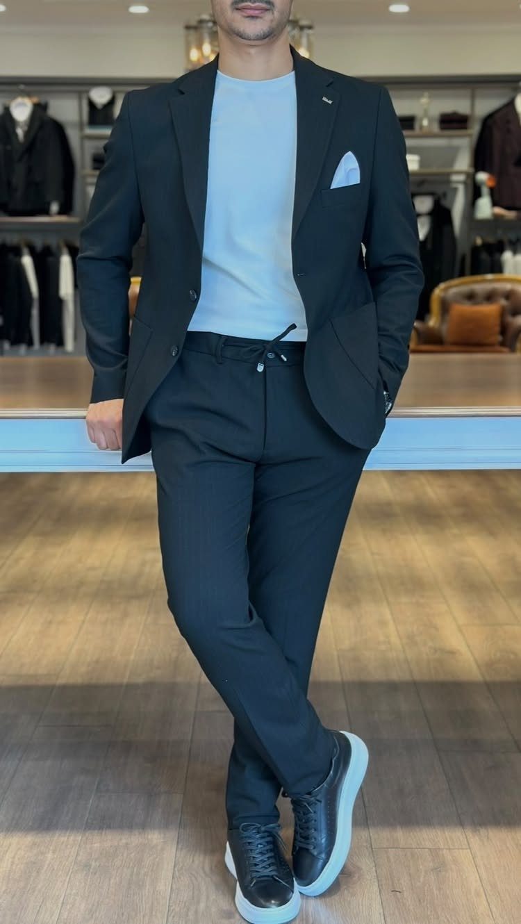 Man posing in a black blazer, light blue t-shirt, black trousers, and black sneakers.
