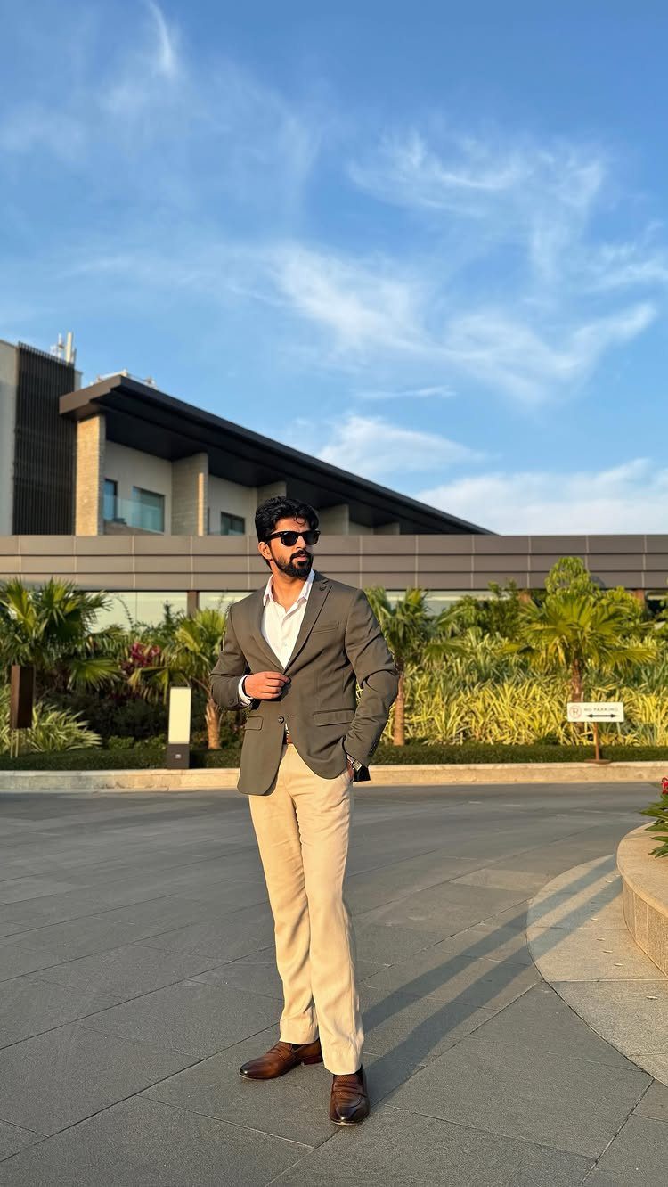 A man posing in a grey blazer, white shirt, and beige trousers outdoors.