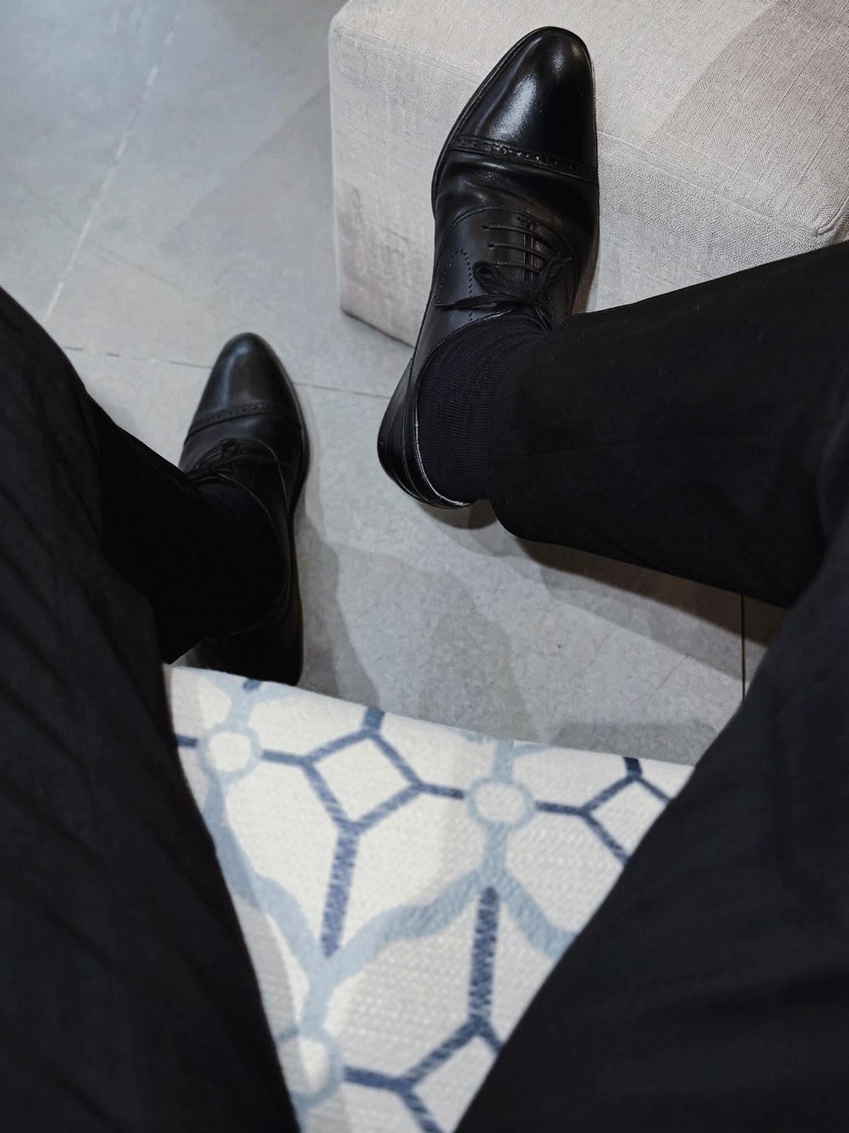 Black leather closed-toed dress shoes worn with black trousers and socks.