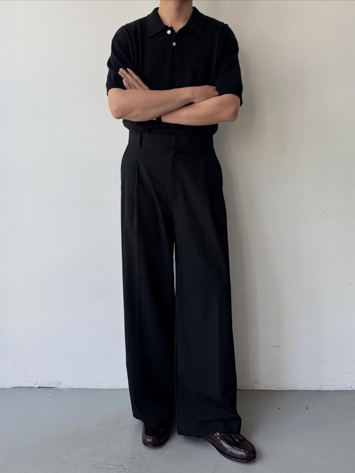 A person wearing a black polo shirt and wide-leg black trousers with brown shoes.