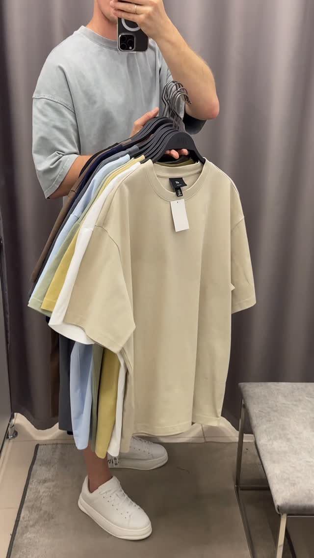 A person holding a collection of colorful oversized t-shirts on hangers.