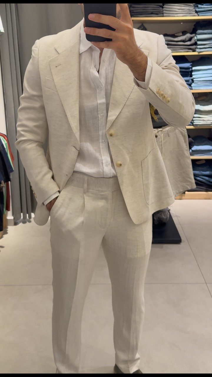 Man in a light beige linen suit and white shirt posing for a mirror selfie.