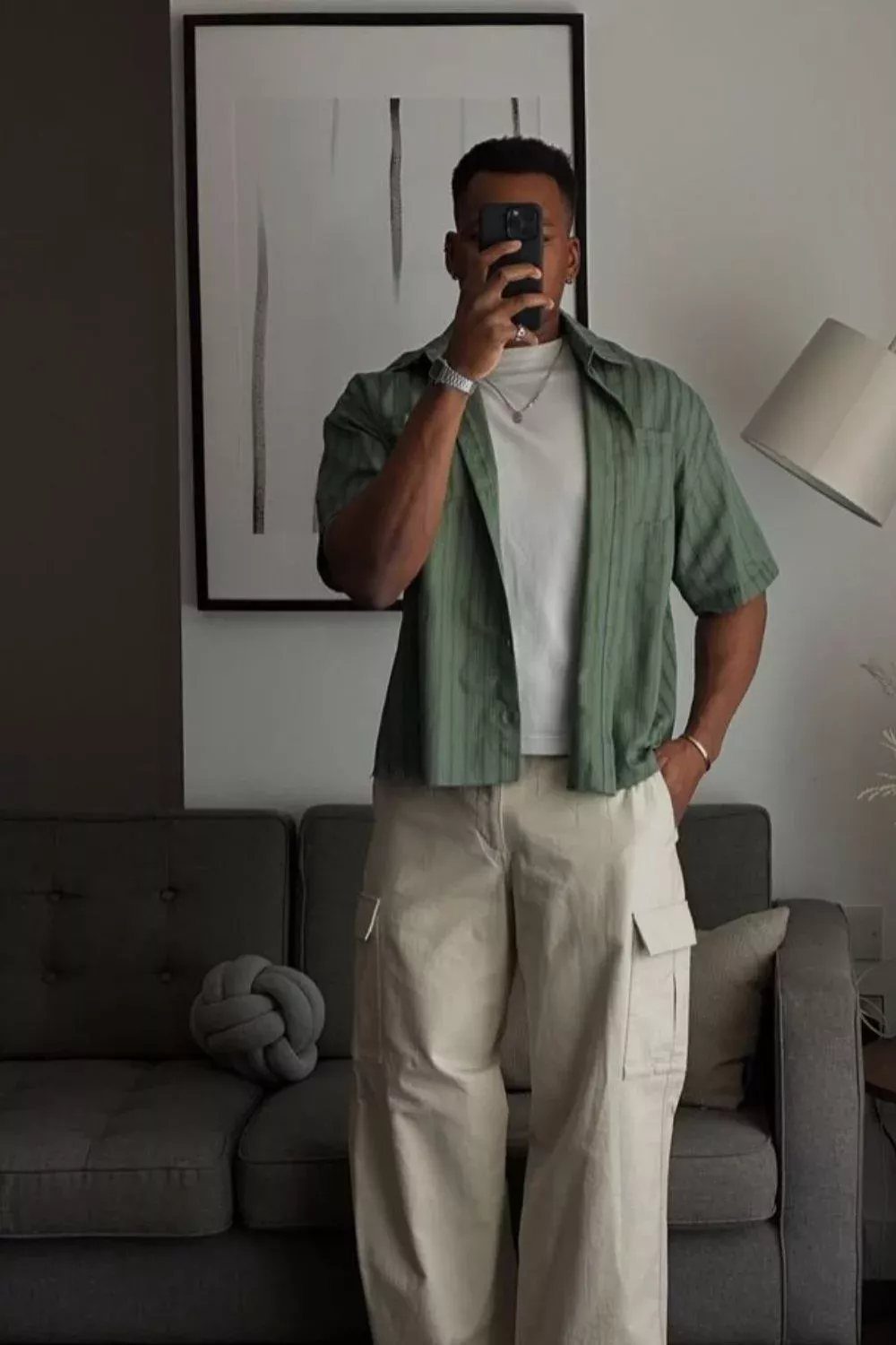 Man in a mirror selfie wearing a loose green shirt and baggy cream cargo trousers.