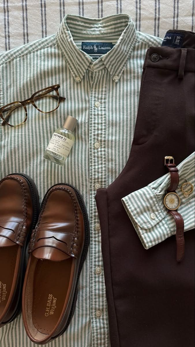 Flat lay of a striped shirt, brown trousers, loafers, glasses, perfume, and a wristwatch.