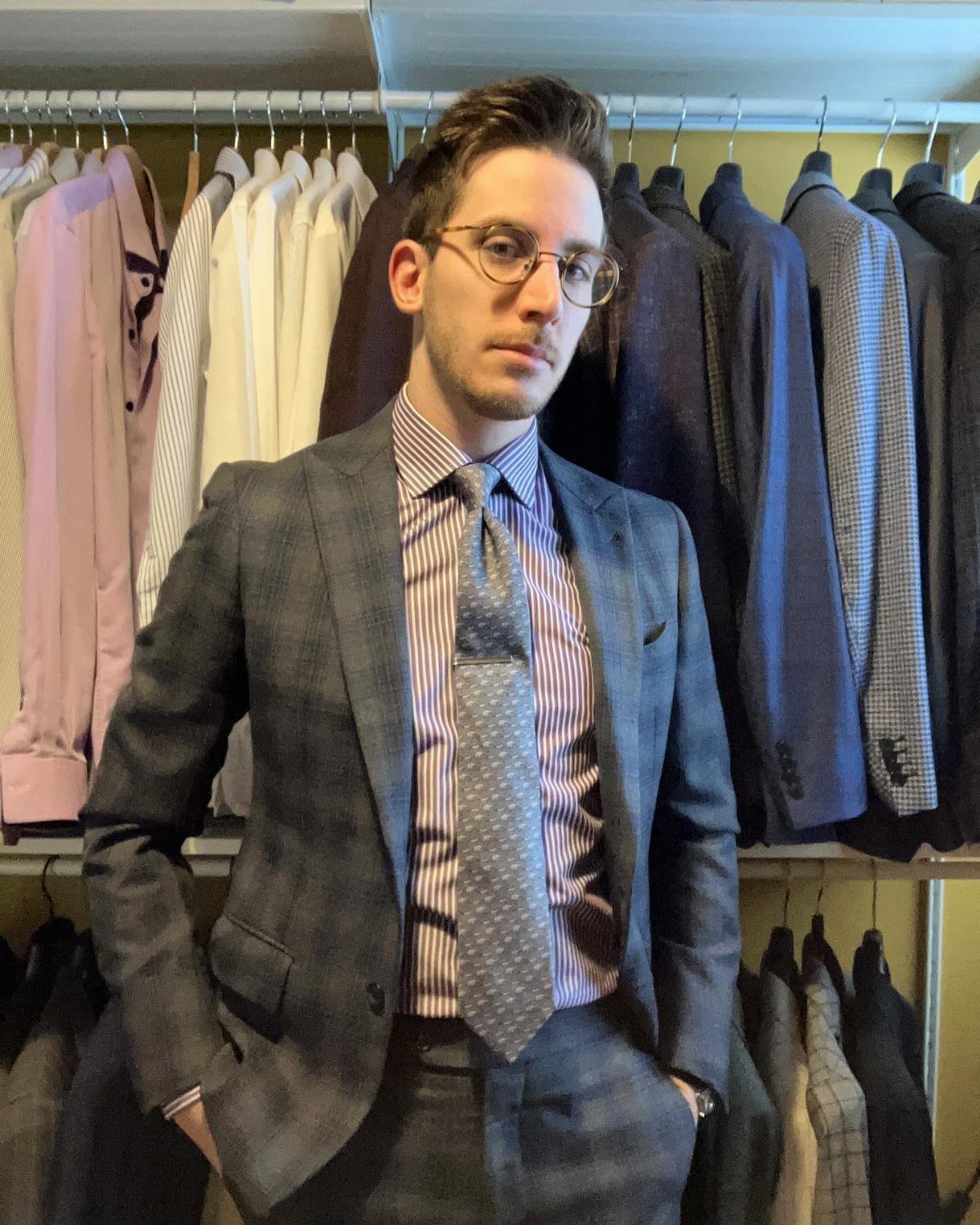 A man in a grey patterned suit and striped shirt wearing a grey patterned tie.