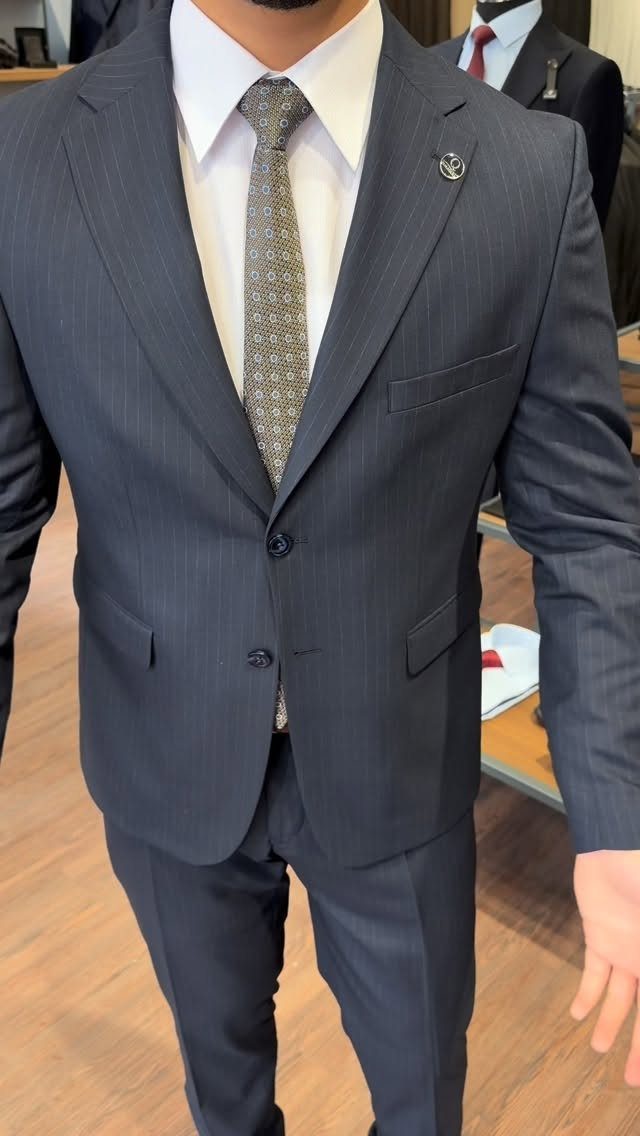 A man wearing a navy pinstripe suit, white shirt, and patterned grey tie.