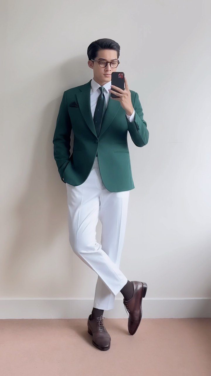 A man in a green blazer, white shirt, tie, and white trousers posing for a selfie.