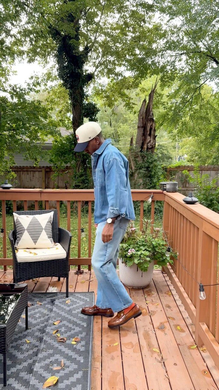 A man in denim clothing and a white cap wearing brown leather loafers on a wooden deck.
