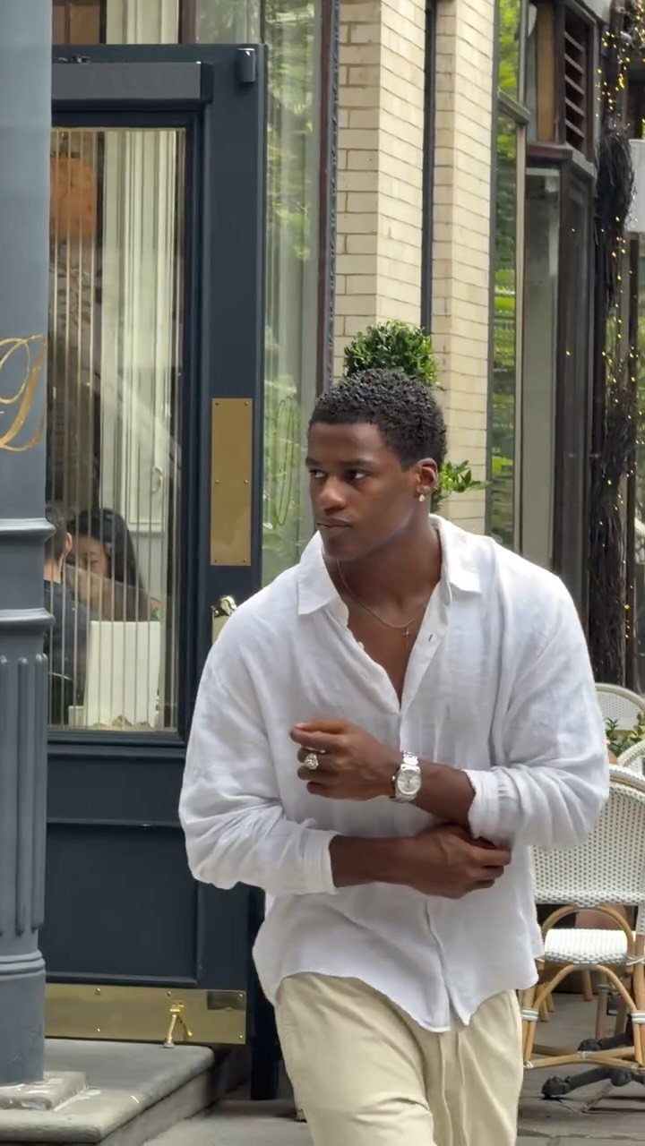A man in a white linen shirt and beige trousers standing outside a building.