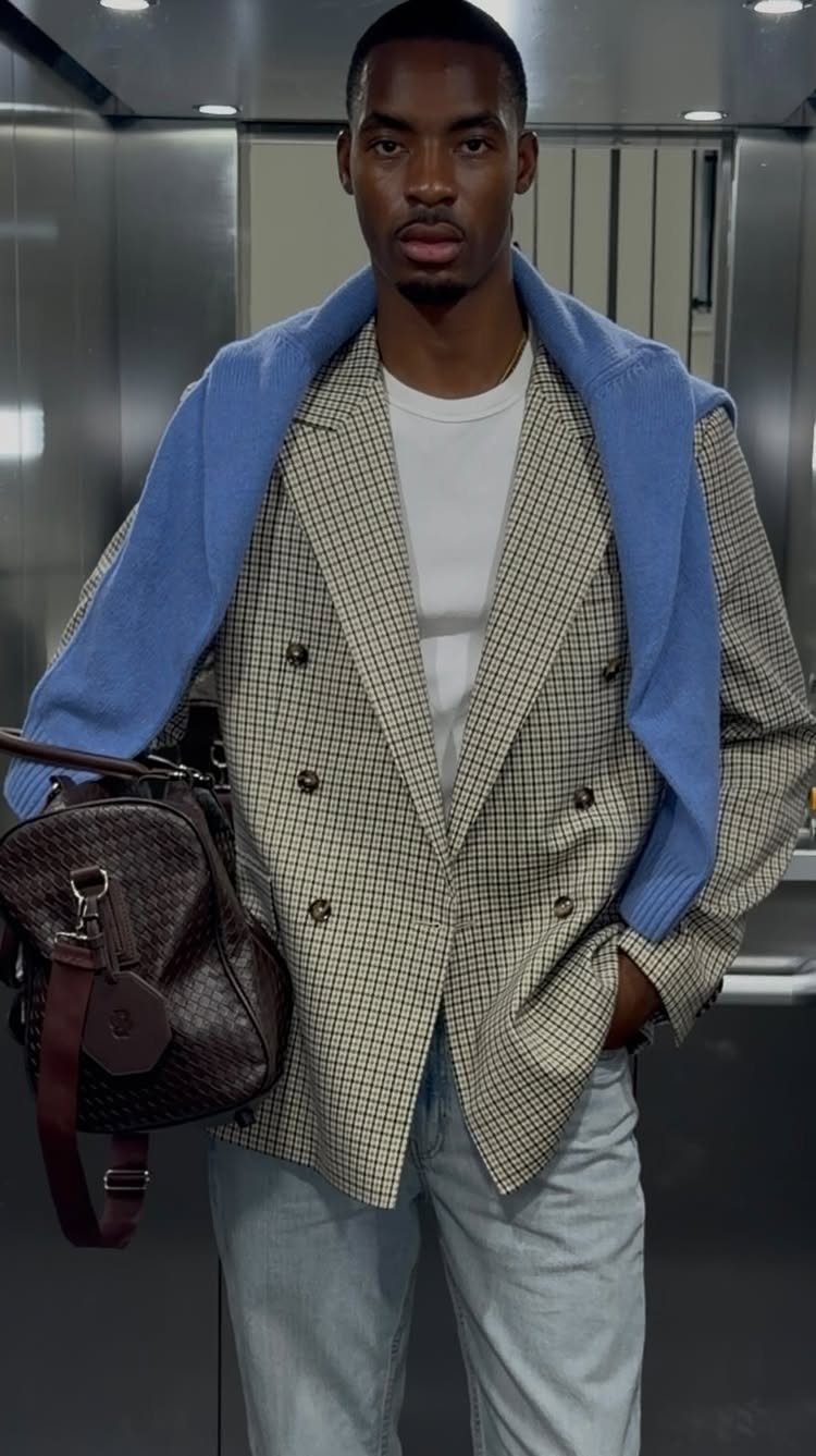 Man wearing a beige checkered blazer, white t-shirt, and blue sweater draped over his shoulders.