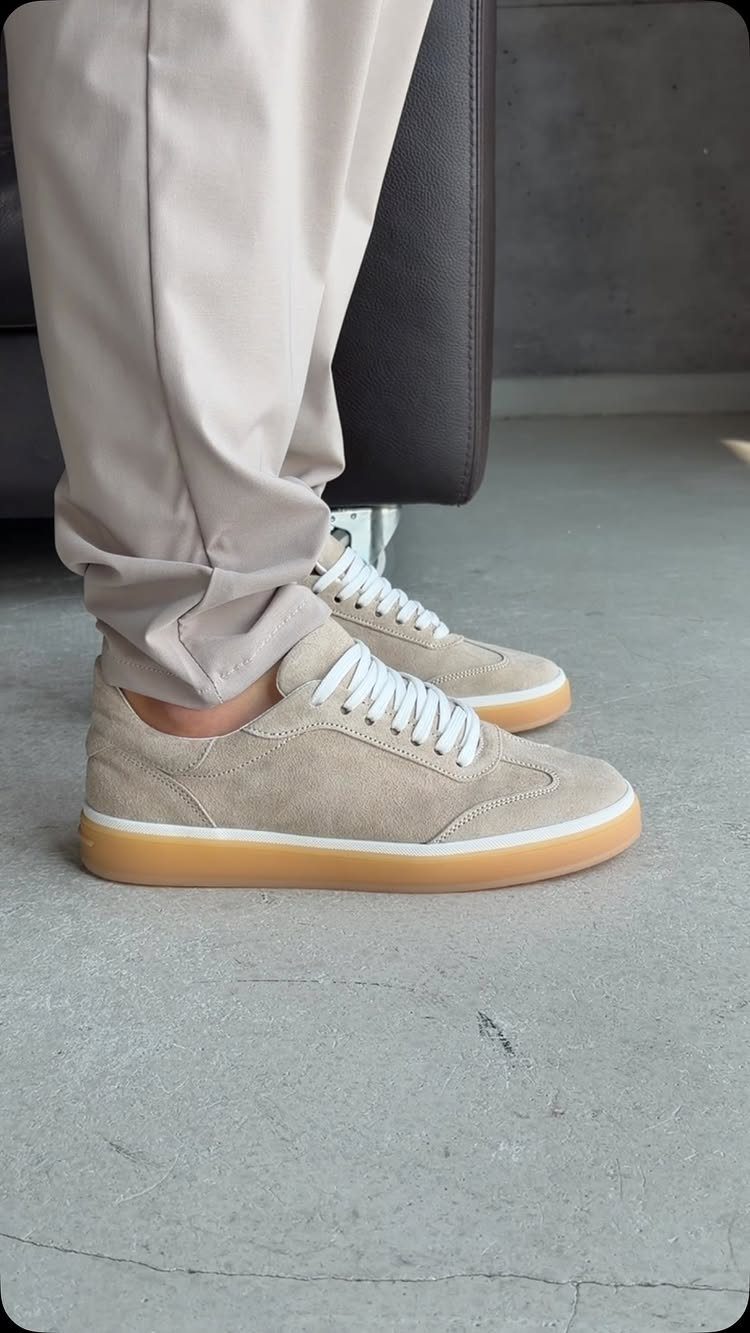 Tan suede minimalist trainers with white laces and gum soles worn with beige trousers.