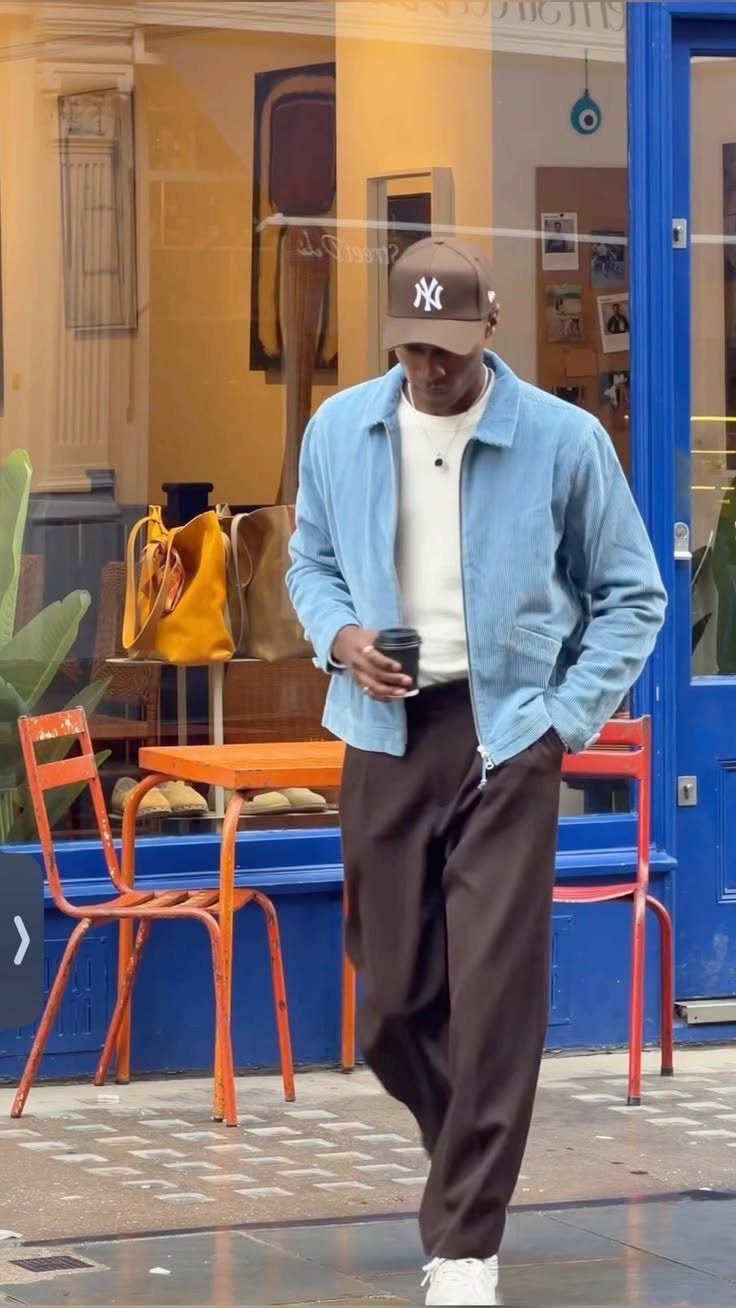 Man walking in a light blue jacket, white shirt, and dark brown trousers outdoors.
