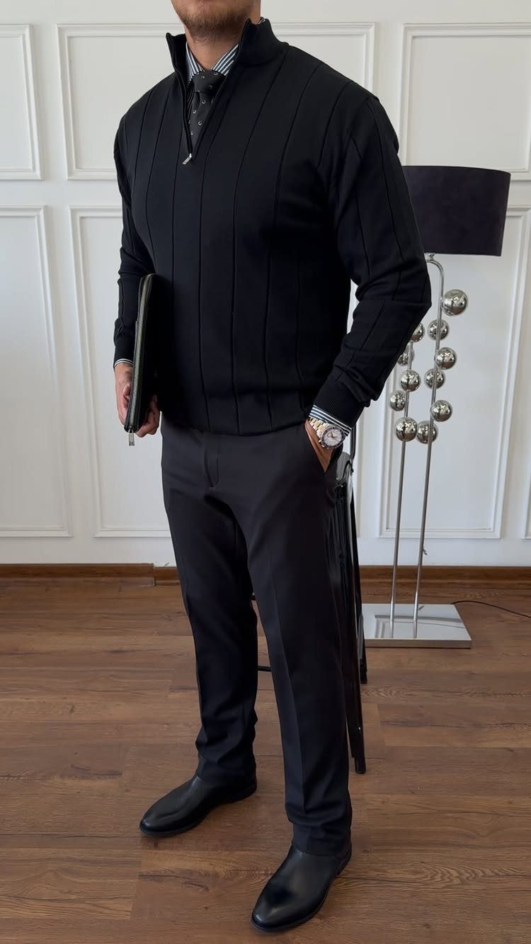 A man in black business casual attire standing in a room with a lamp.