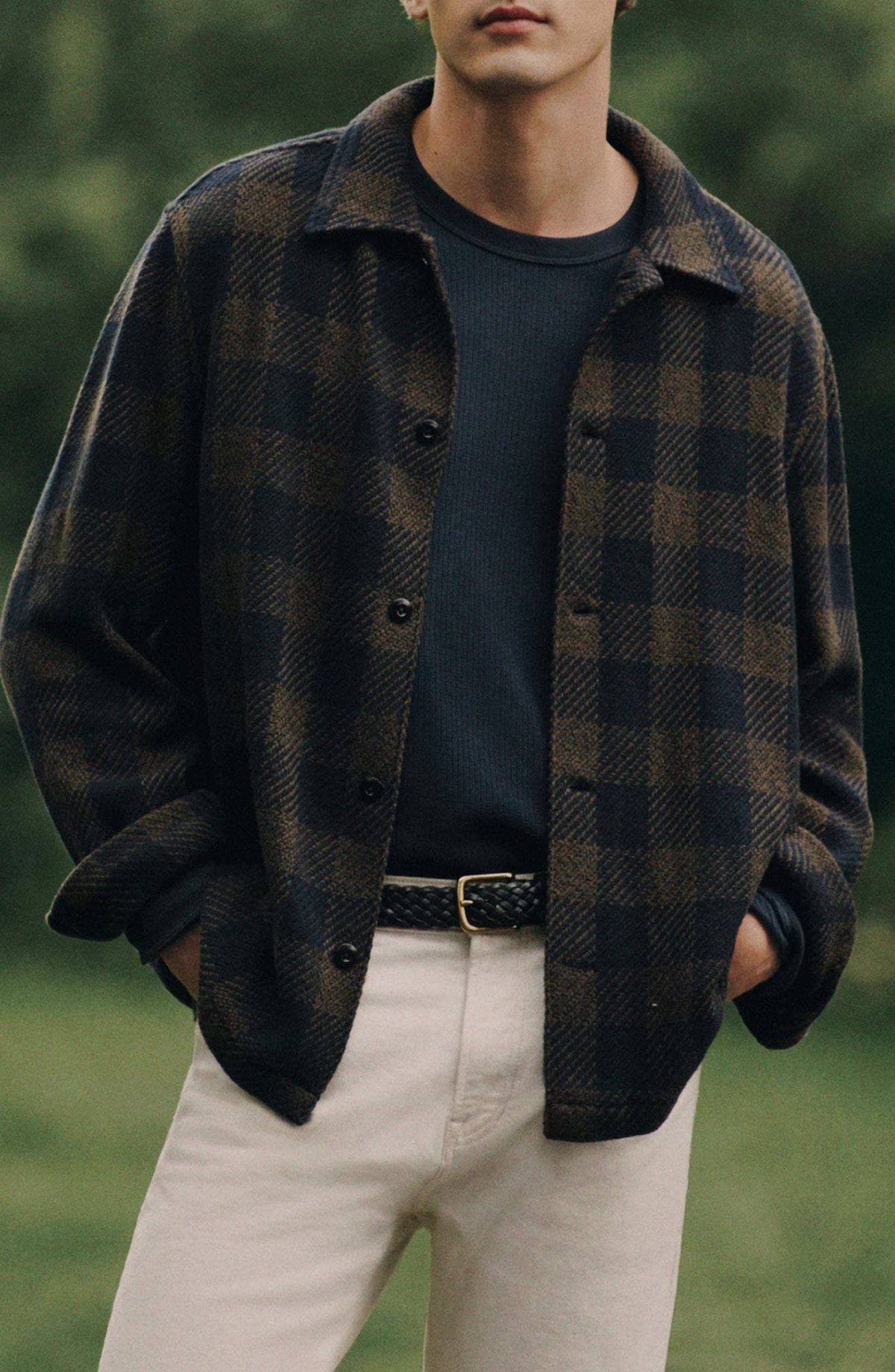 Man wearing a dark plaid jacket over a navy t-shirt and cream trousers.