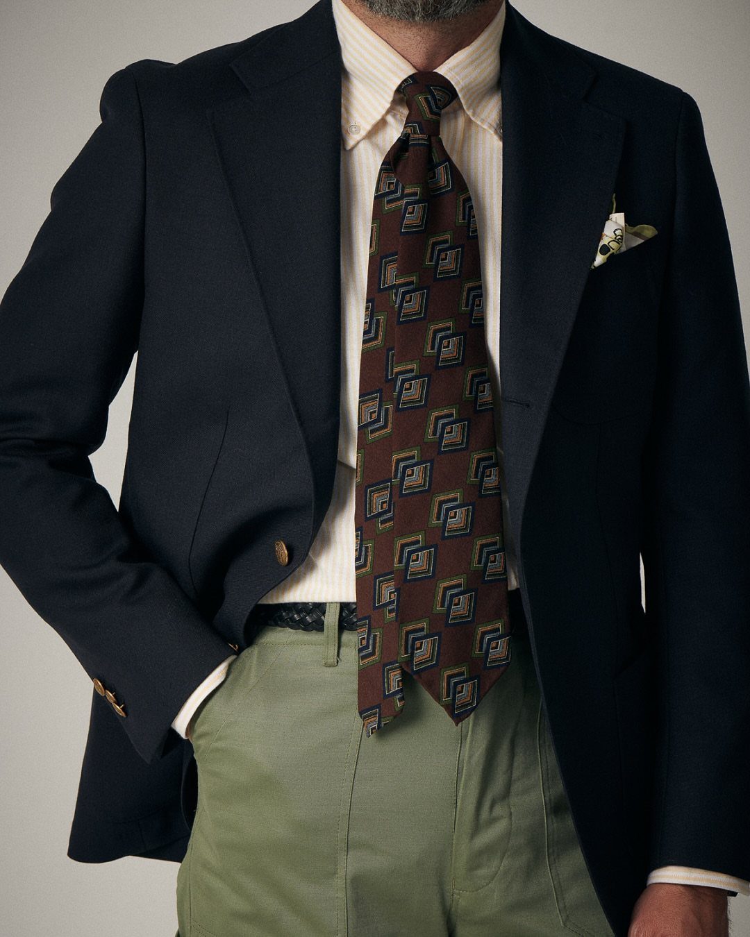 Man wearing a navy sports coat, striped shirt, patterned tie, and olive green chinos.