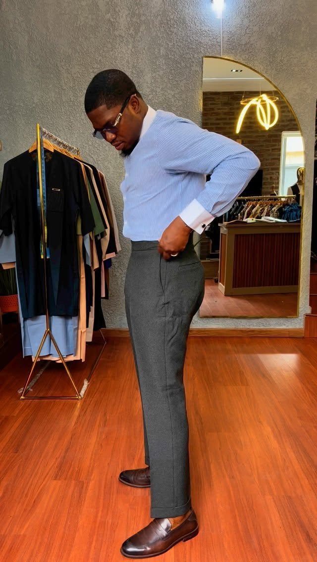 A man wearing a blue striped shirt and dark grey tailored trousers in a clothing store.