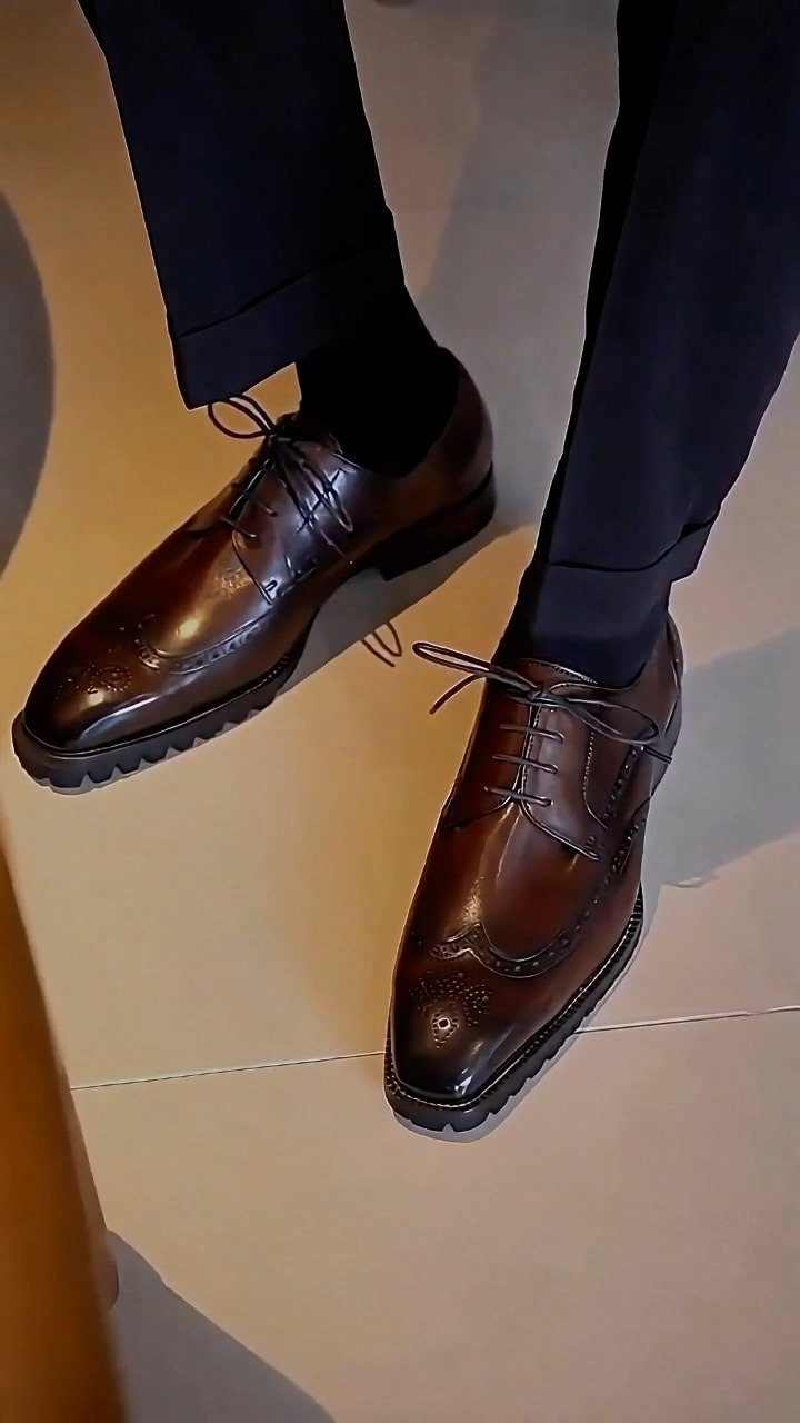 Brown leather derby shoes with brogue detailing worn with navy trousers and black socks.
