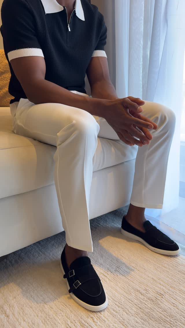 A person wearing a black polo shirt with white trim and white trousers sitting on a sofa.