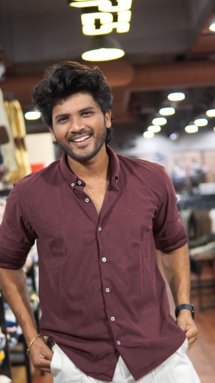 A smiling man wearing a maroon short-sleeved button-down shirt and white pants.