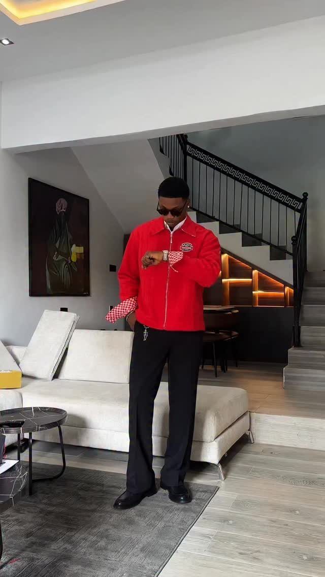 Man in a red jacket and black trousers posing in a modern living room.