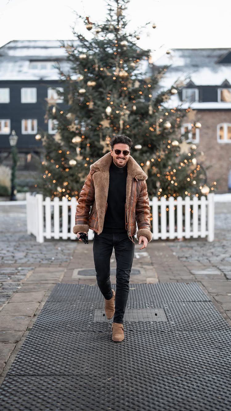 A man in a shearling jacket and black turtleneck walking past a large Christmas tree.