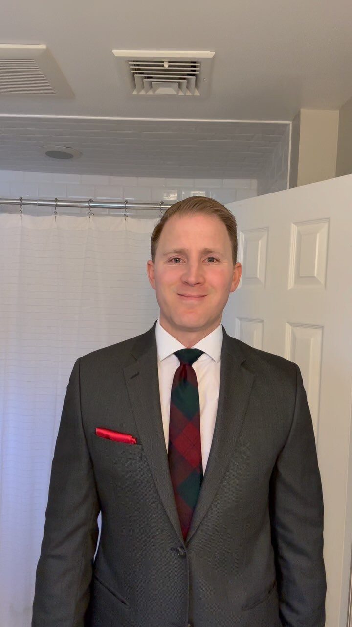 Man in a grey suit wearing a festive red and green plaid tie and pocket square.
