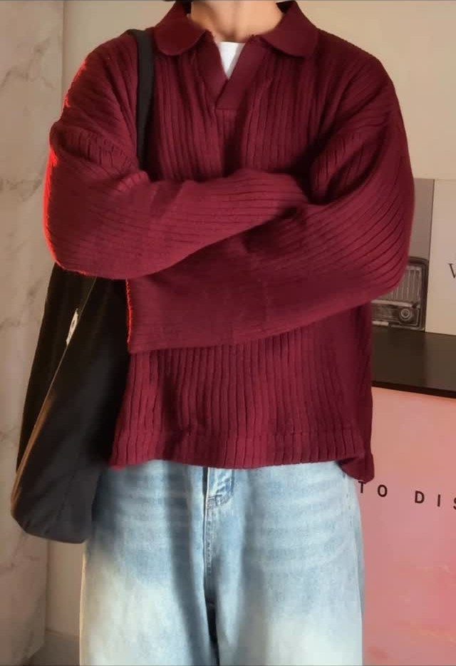 A person wearing a maroon ribbed knit polo sweater and light blue denim jeans.